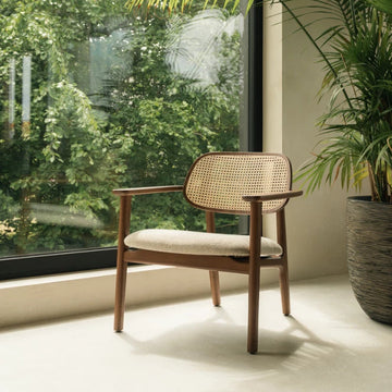 Wooden armchair with woven backrest in a room with large windows and greenery outside

