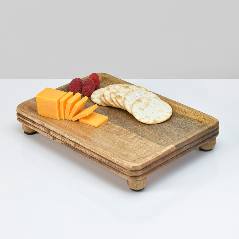 Wooden cheese board with sliced cheese, crackers, and berries on a white background